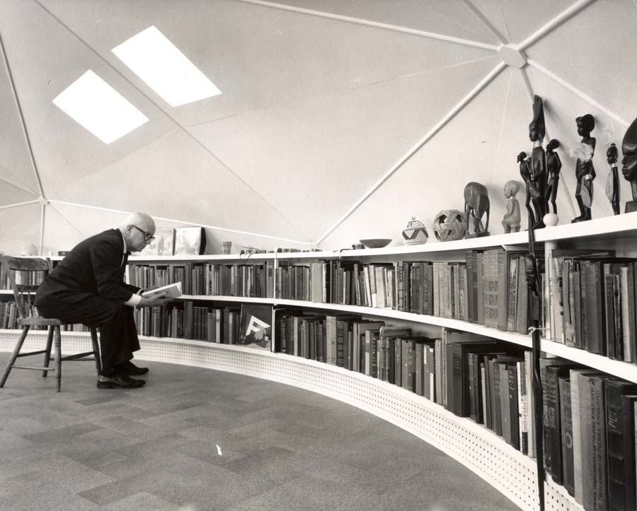 Buckminster Fuller reading a book inside a large and full library in the Dome Home